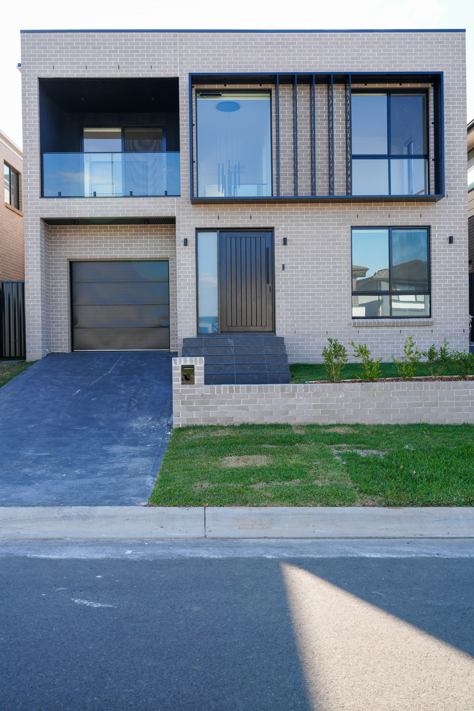 Street frontage of a completed Auzzy Projects home in Sydney's North West, showing the driveway crossing, the fall from the house down to the kerb, and the front setback